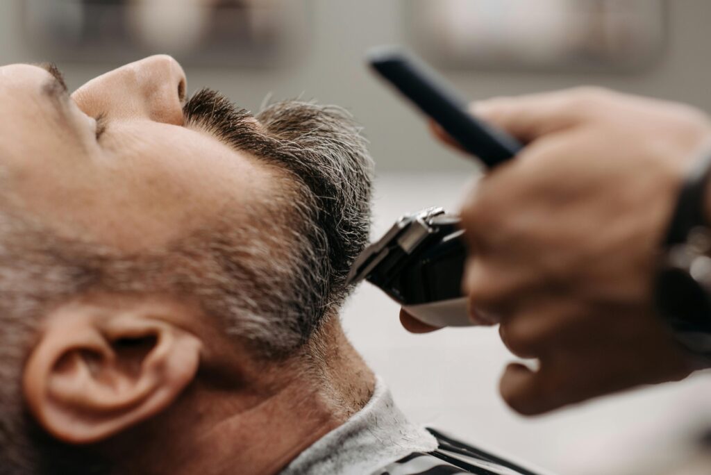 Close-up of a barber using clippers to groom a client's beard in a barbershop.